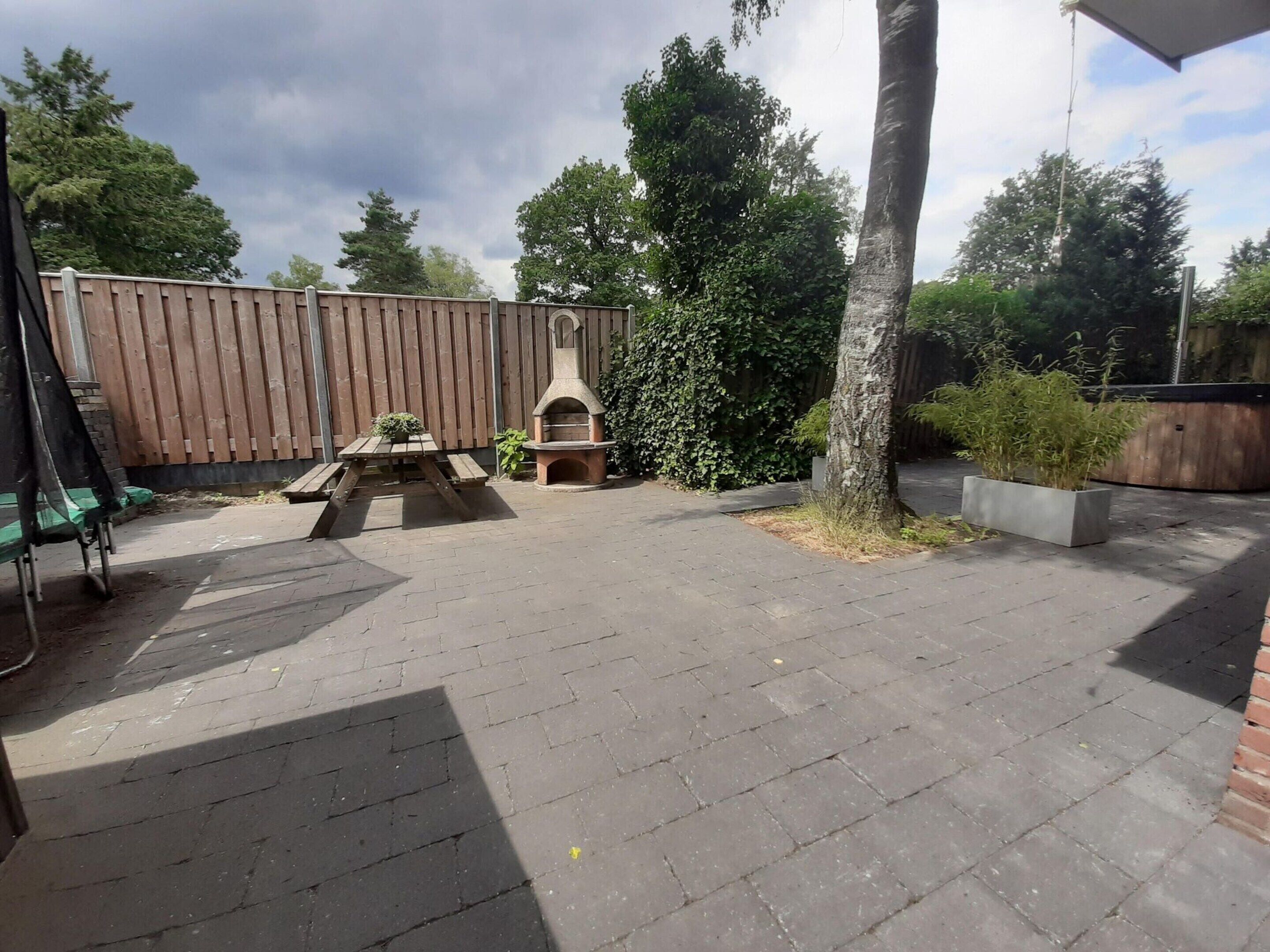A patio area with a brick floor, a wooden table, a barbecue grill, and a wooden fence.