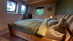 A bedroom with a wooden bed, two windows, a radiator, and a bedside lamp. - Holiday Home in Voorthuizen With Hot Tub (Voorthuizen)