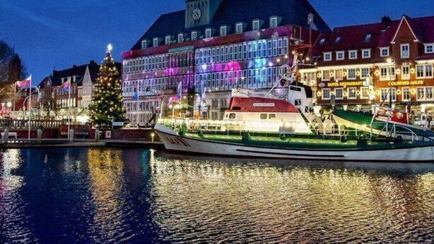 A waterfront hotel with a prominent clock tower, a Christmas tree, and a boat docked in front. - Holiday Home Anje Comfortable Vacation Home (Krummhoern)