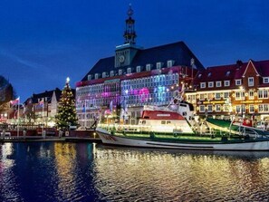 A waterfront hotel with a prominent clock tower, a Christmas tree, and a boat docked in front. - Holiday Home Anje Comfortable Vacation Home (Krummhoern)
