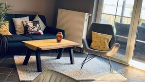 A modern living room with a dark green sofa, a wooden coffee table, a black armchair, and a large window providing a view of the outdoors. - Holiday Home Anje Comfortable Vacation Home (Krummhoern)