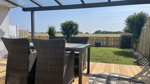 An outdoor patio with wicker furniture and a round table, overlooking a fenced yard with trees and a clear sky. - Holiday Home Anje Comfortable Vacation Home (Krummhoern)