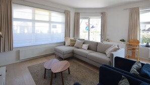 A modern living room with a sectional sofa, a blue armchair, and a small wooden table. - Apartment Near Ostend Beach (De Haan)