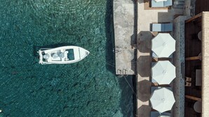 Vista aérea de un barco amarrado en un muelle, con una zona de playa que incluye sombrillas y asientos.