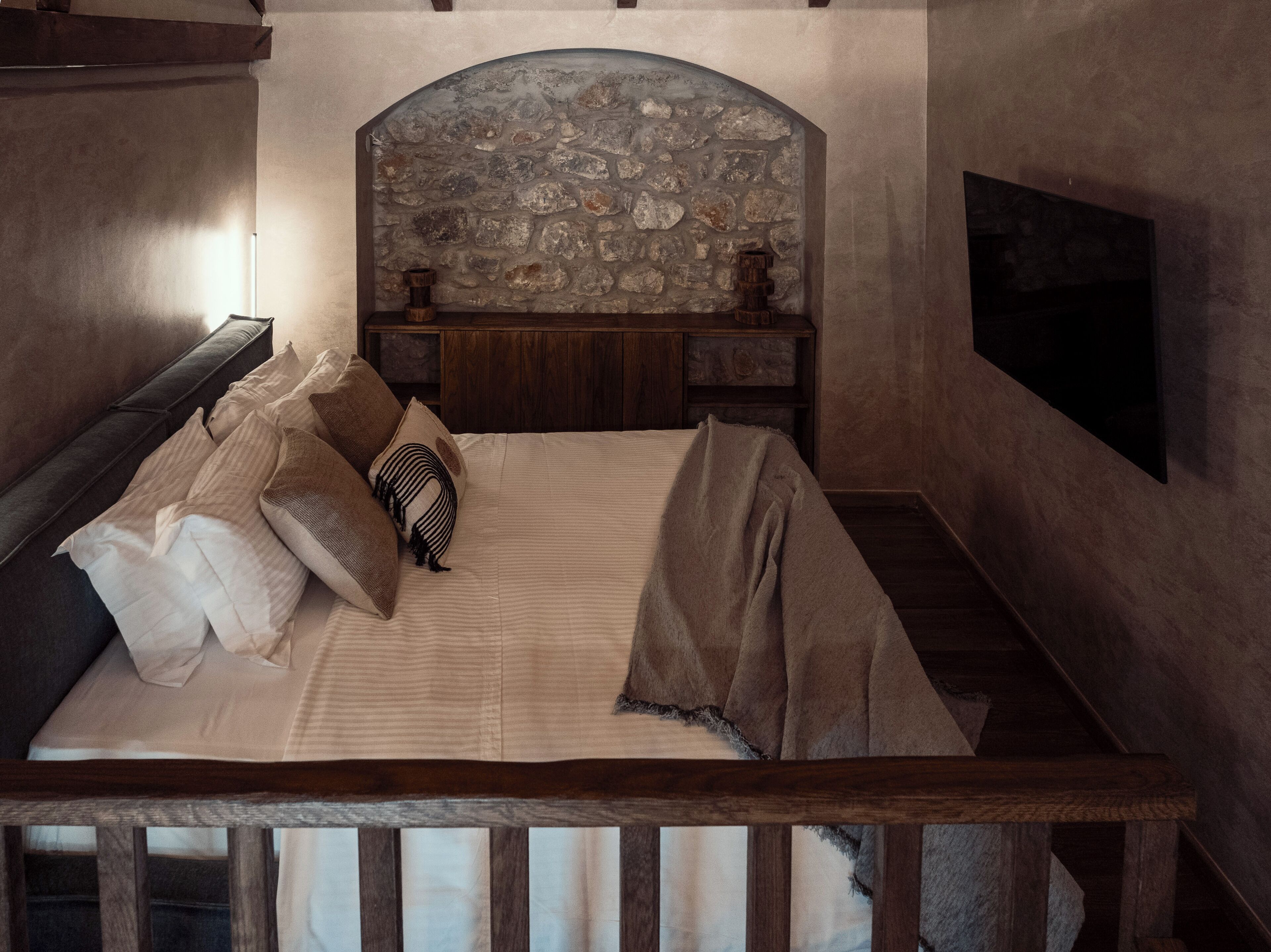 Een slaapkamer met een stenen hoofdbord, een houten bedframe en een nachtkastje met een lamp.
