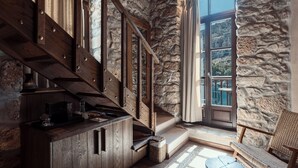 Un interior rústico con una escalera de madera, paredes de piedra, una zona de estar acogedora y vistas a un paisaje montañoso.