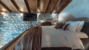 A bedroom with a stone wall, wooden ceiling beams, a bed with white linens, and a mounted TV.