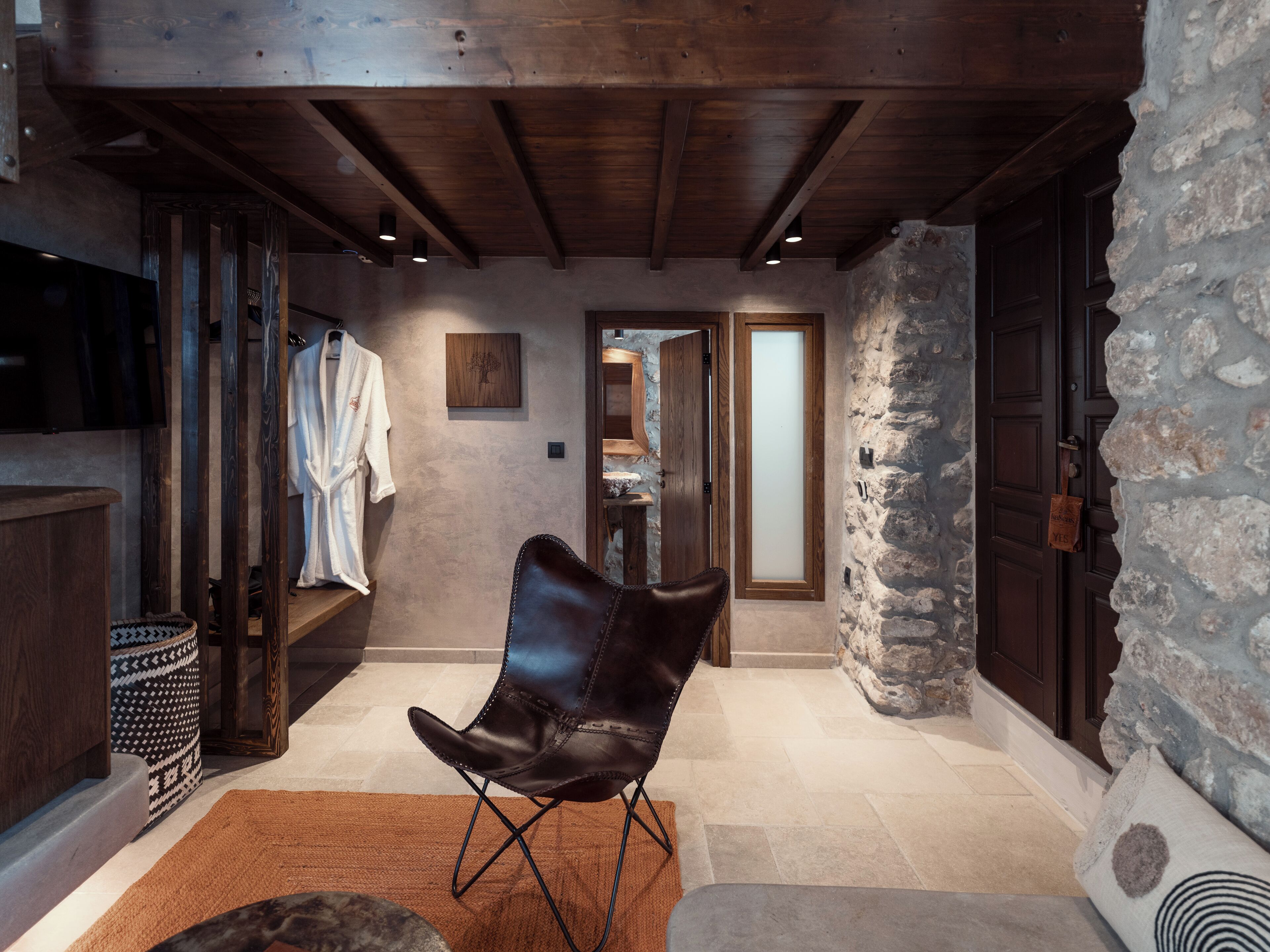 A modern interior with a stone wall, wooden ceiling beams, a leather chair, and a large mirror.