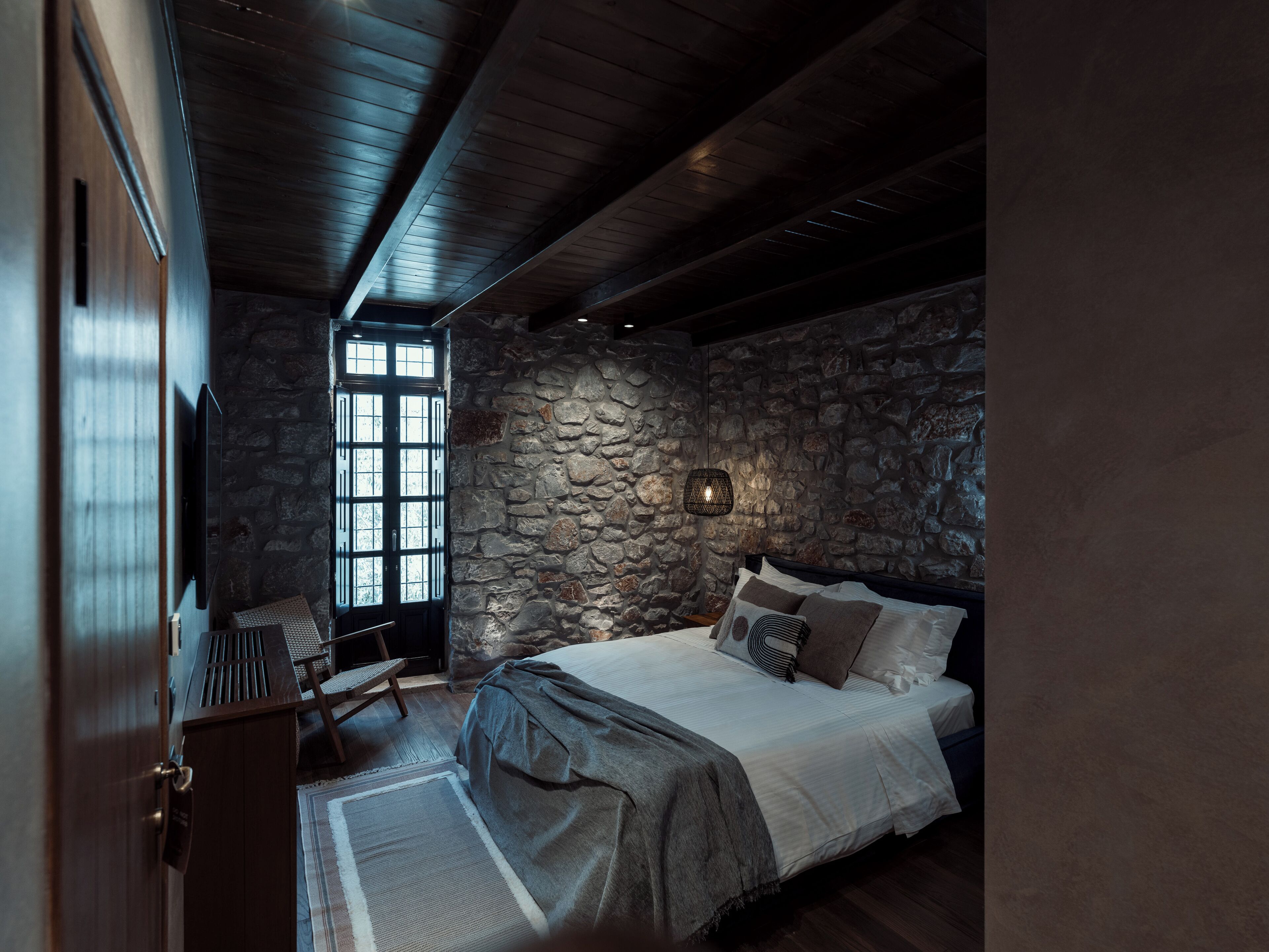 Une chambre avec un mur en pierre, un lit avec des oreillers, un bureau et une chaise.