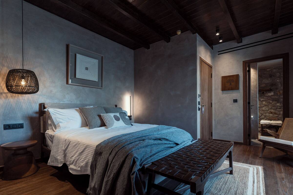 Een moderne slaapkamer met een groot bed, een bankje, een nachtkastje en een wandlamp.