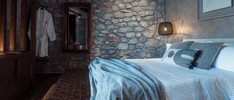A bedroom with a stone wall, a wooden bench, a bed with pillows, and a hanging robe.