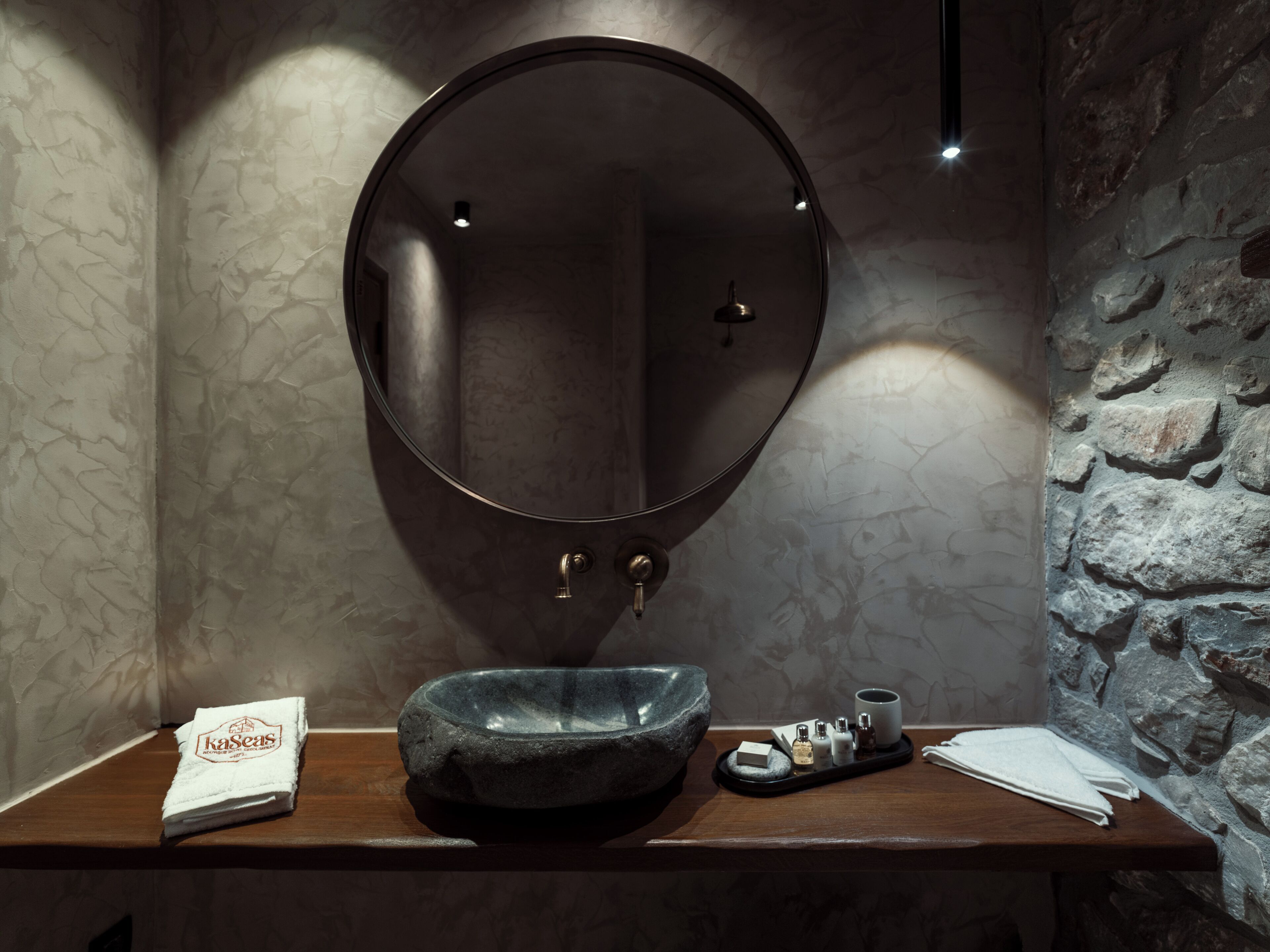Un baño con un espejo redondo, un lavabo de piedra y un tocador de madera.