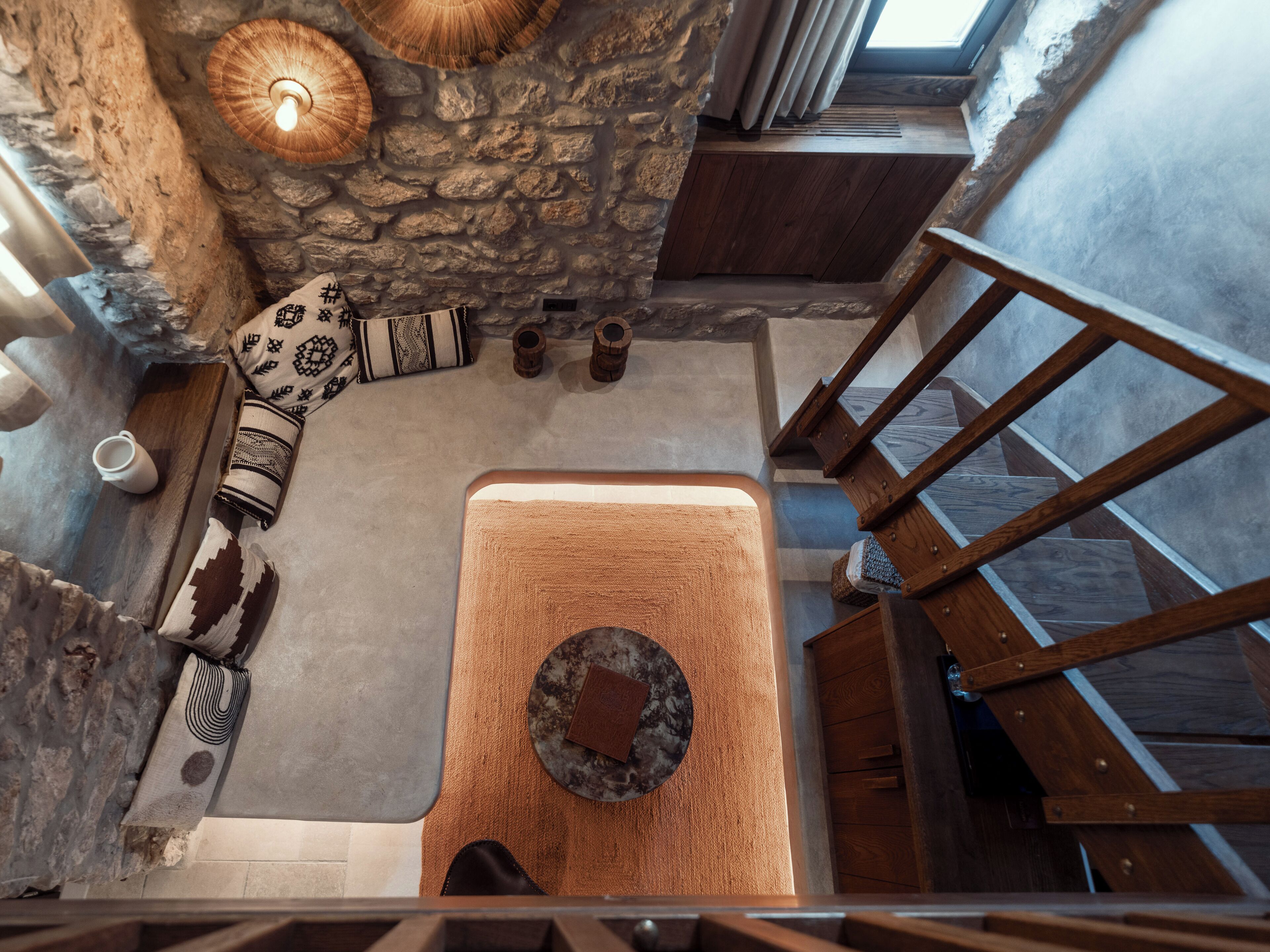 Una habitación con techos altos, una pared de piedra, una escalera de madera y una zona de estar central con una mesa y sillas.