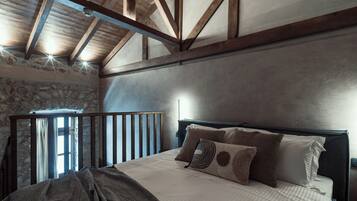 A bedroom with a wooden ceiling, stone wall, and a bed with multiple pillows.