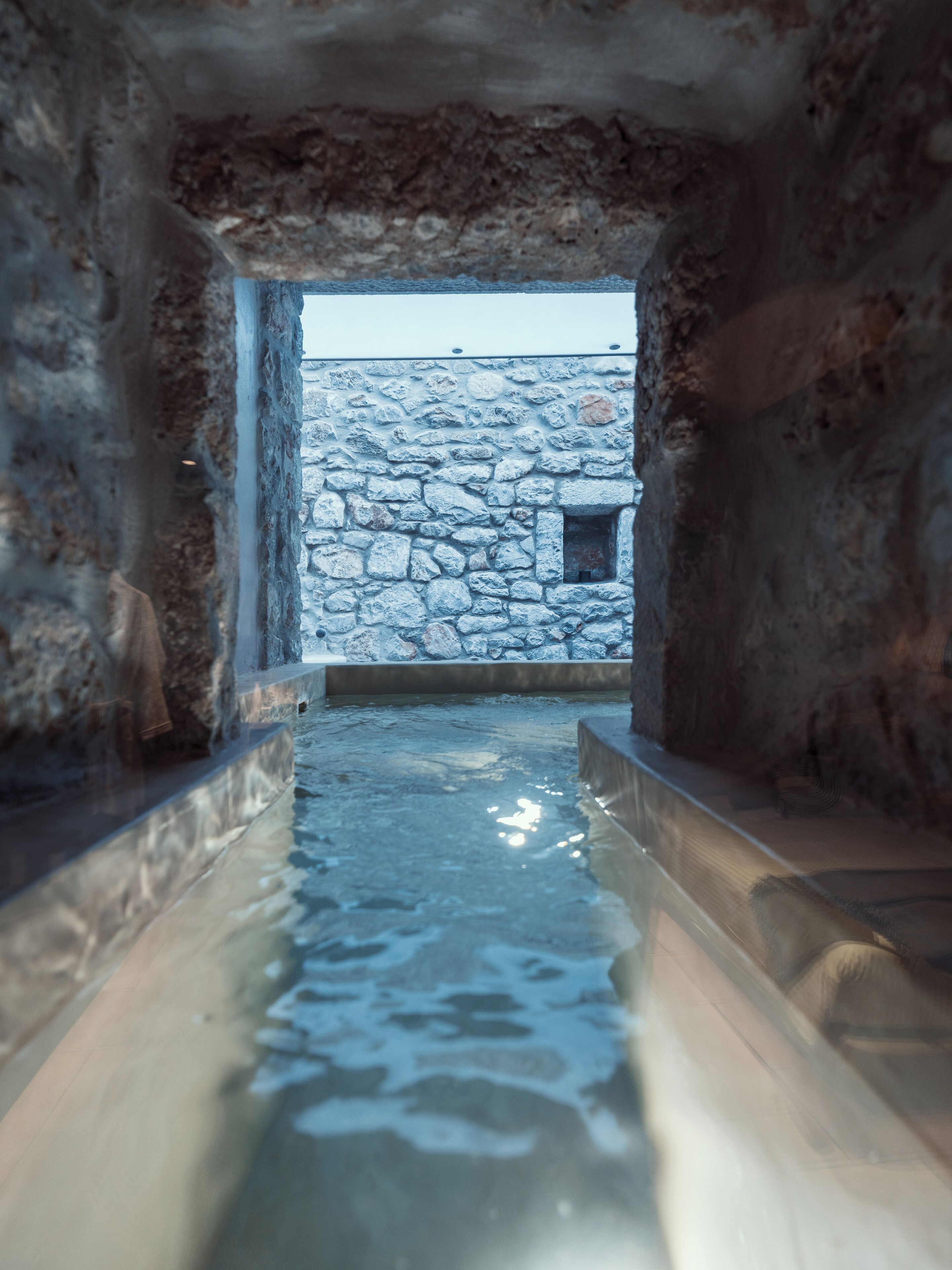 A stone-walled pool with a clear view of a stone building outside.