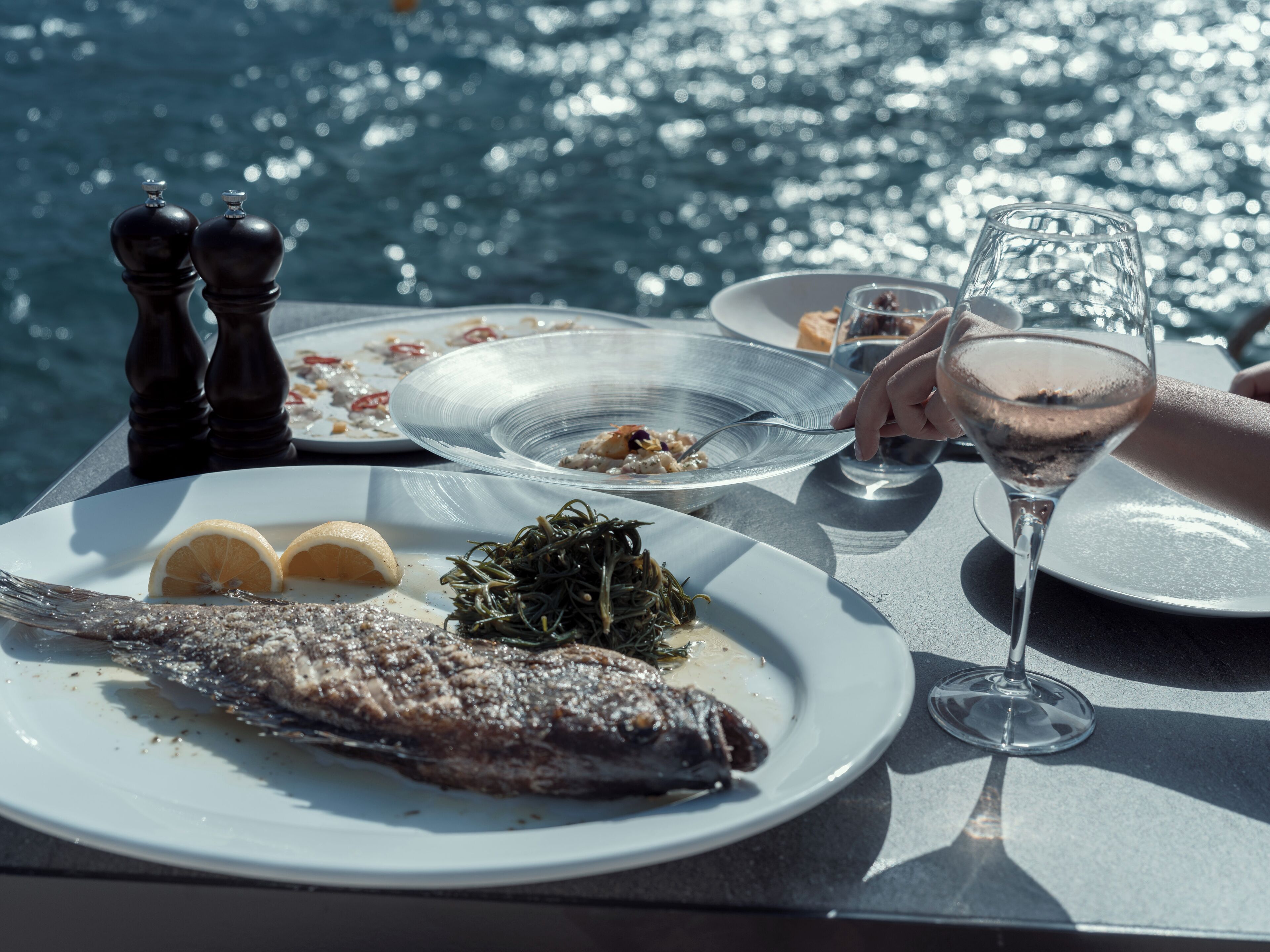 Une table à manger avec des assiettes remplies de nourriture, un verre de vin et une vue sur l’eau.