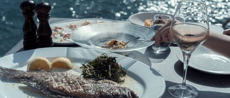 Une table à manger avec des assiettes remplies de nourriture, un verre de vin et une vue sur l’eau.