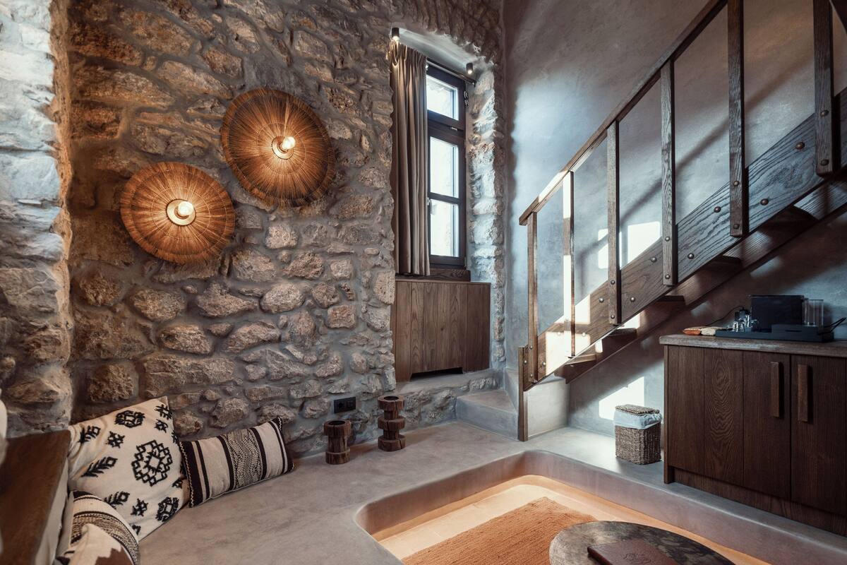Een modern interieur met een stenen muur, een houten trap en een zithoek met gestreepte kussens.