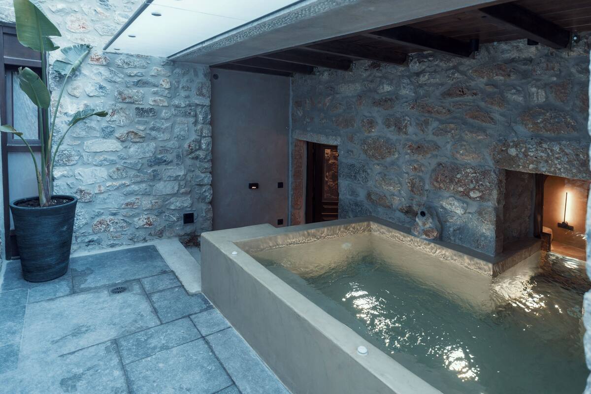Een kamer met stenen muren, een bubbelbad, een potplant en een deur naar een andere ruimte.