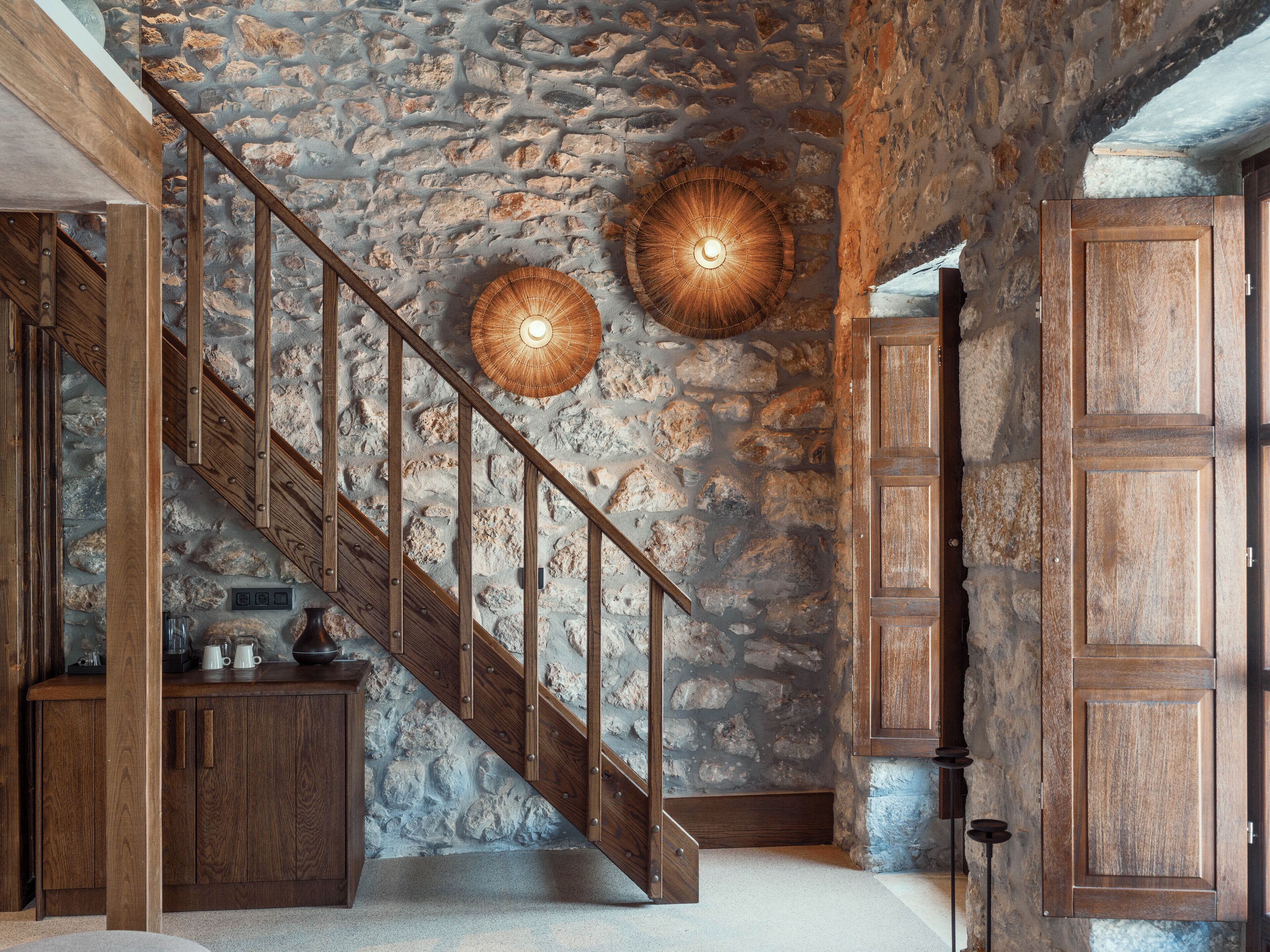 A rustic interior with a stone wall, wooden staircase, and built-in wooden cabinets.