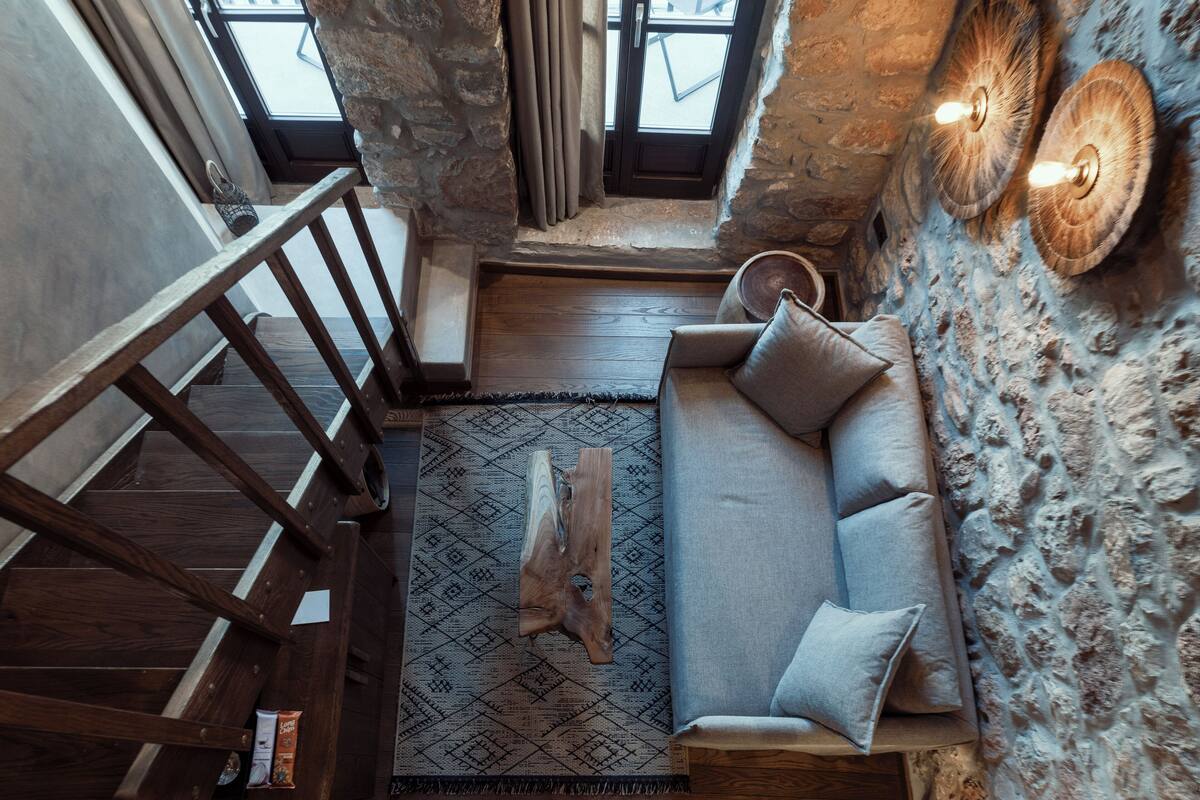Een loft-achtige woonruimte met een stenen muur, een houten trap en een ingebouwde bank met kussens.