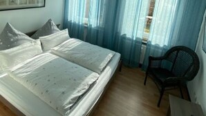 A bedroom with a bed, a chair, a small table, and a window with curtains. - Holiday Apartment Luna (Ruedesheim am Rhein)