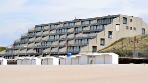 Ein modernes Gebäude mit einer einzigartigen geometrischen Fassade, mehreren Balkonen und einem Flachdach.