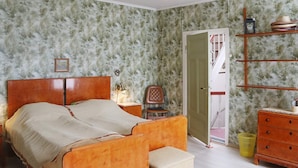 A bedroom with a wooden bed, a nightstand, a chair, a dresser, and a shelf with hats. - 5 Person Holiday Home in Risor (Risør)