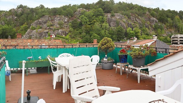 A rooftop terrace with white plastic chairs and tables, surrounded by greenery and a view of a mountainous landscape. - 5 Person Holiday Home in Risor (Risør)