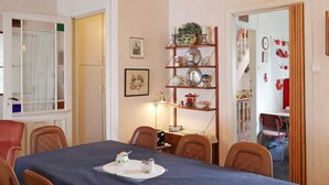 A dining area with a table set for four, chairs, a chandelier, and a shelf with dishes and a clock.