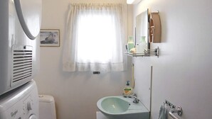 A compact bathroom with a toilet, a sink, a mirror, and a window with a curtain.