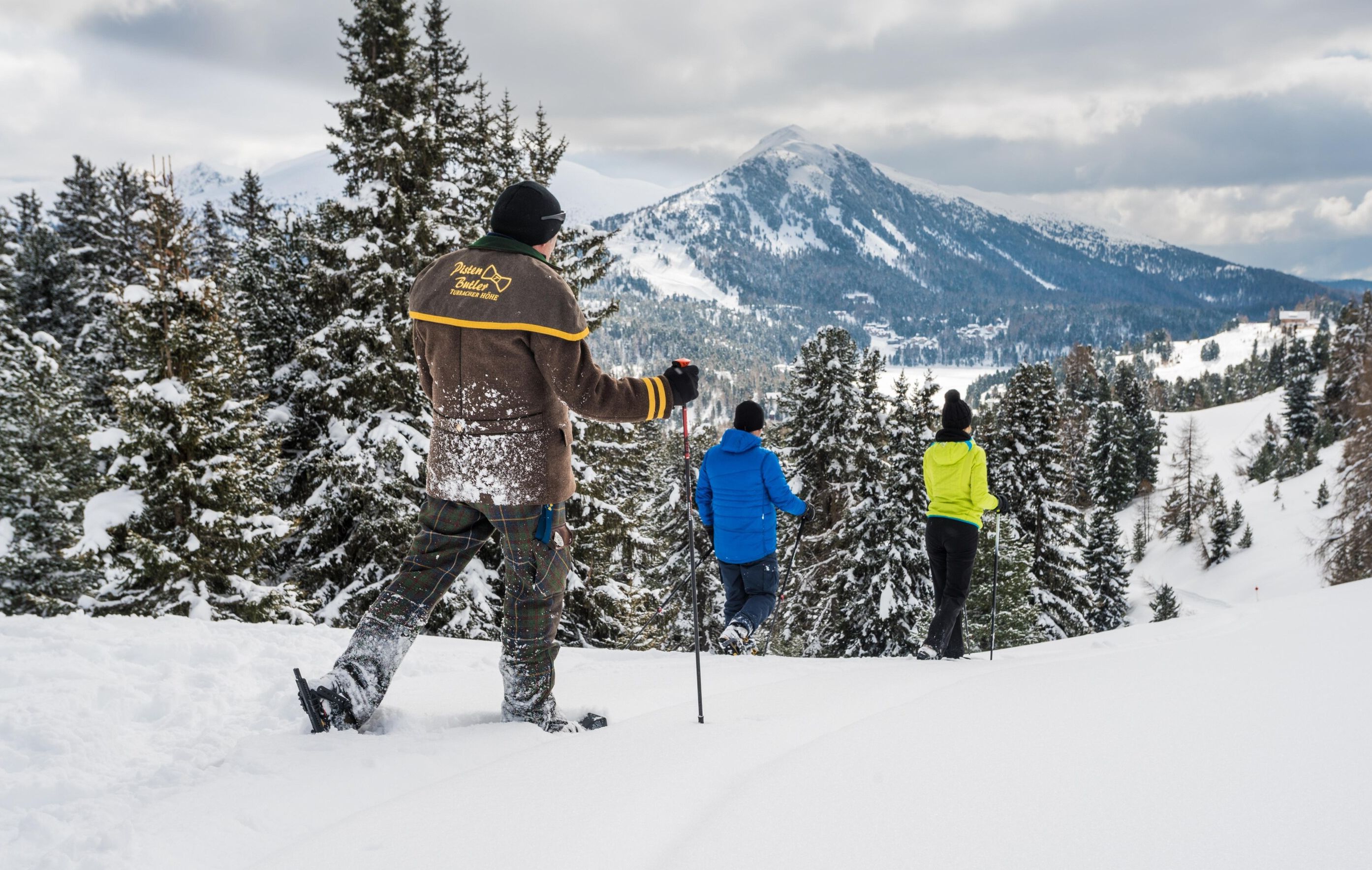 A snowy mountain landscape with a group of people skiing.
