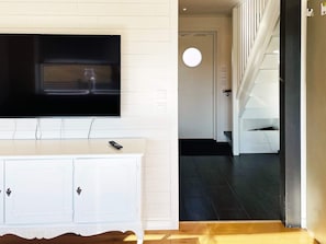 A modern living room with a flat-screen TV mounted on the wall, a white cabinet with drawers, and a staircase leading to another level. - 4 Star Holiday Home in Fagerfjall (Fagerfjäll)