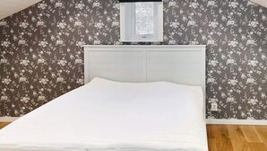 Ein Einzelbett mit weißem Kopfteil in einem Zimmer mit floralem Wandpapier und Holzböden.