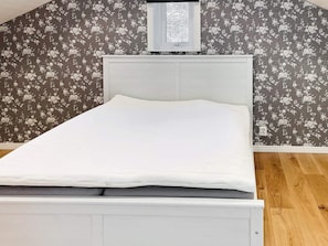 Een eenpersoonsbed met een wit hoofdeinde in een kamer met bloemenbehang en houten vloer.