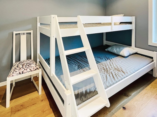 Una cama litera con escalera, una silla con cojín estampado y una ventana.