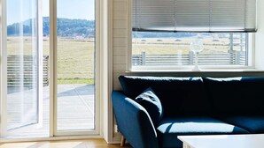 Ein Zimmer mit einem blauen Sofa, einem weißen Tisch und Blick auf ein grünes Feld durch ein großes Fenster.
