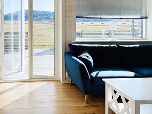 Een kamer met een blauwe bank, een witte tafel en uitzicht op een grasveld door een groot raam.