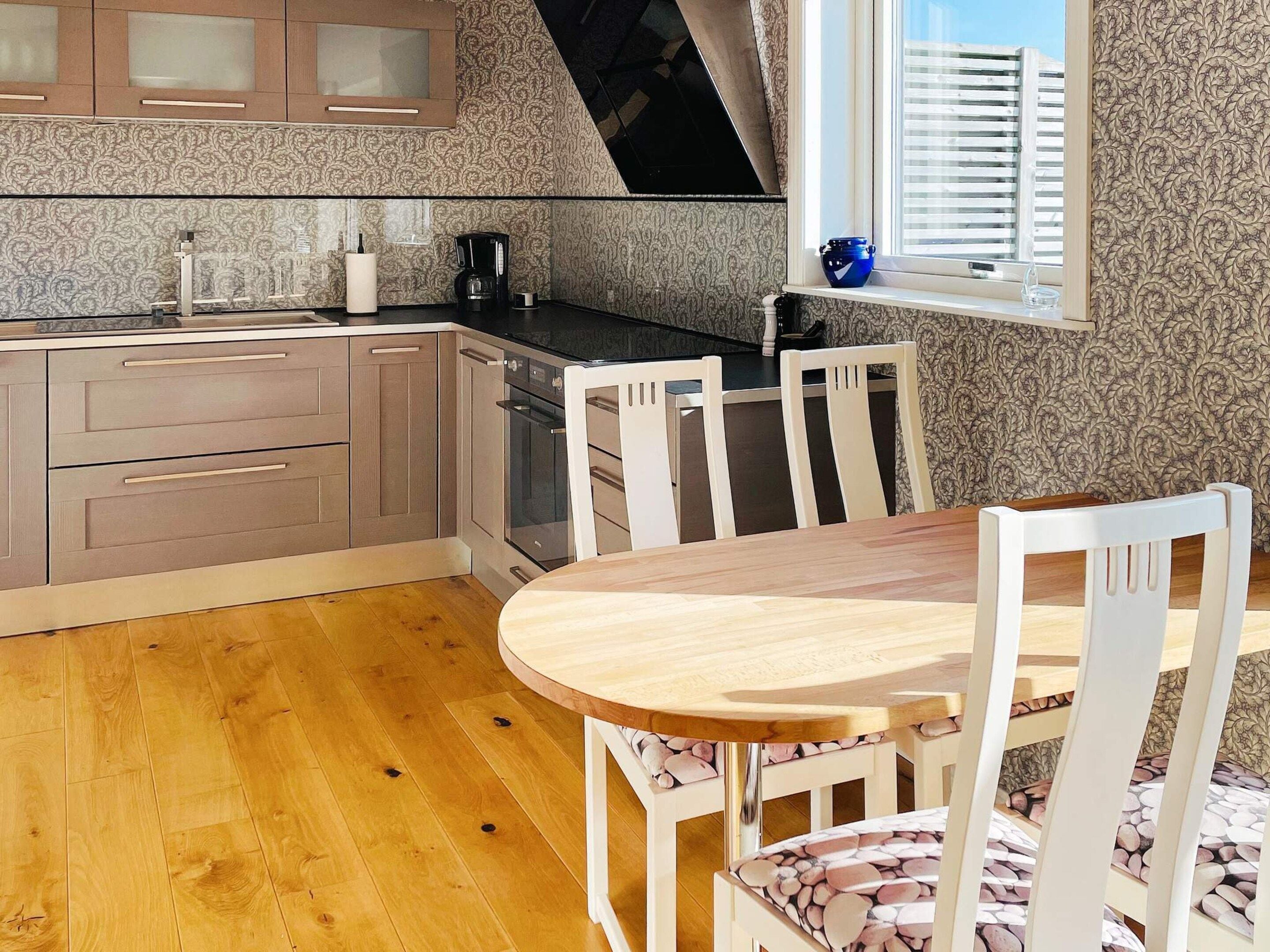A modern kitchen with wooden cabinets, a built-in oven, and a dining area with a wooden table and white chairs.