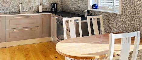 Una cocina moderna con armarios de madera, horno integrado y comedor con mesa de madera y sillas blancas.