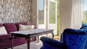 A living room with a purple sofa, a blue armchair, a wooden coffee table, and a patterned wallpaper. - 4 Person Holiday Home in Odsmal (Oedsmal)