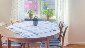 A round wooden table with a striped tablecloth, surrounded by wooden chairs with striped cushions. There are two potted plants on the windowsill. - 4 Person Holiday Home in Odsmal (Oedsmal)