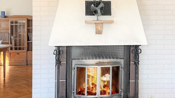 A fireplace with a white mantel and a metal grate, flanked by wooden mantels and a brick wall. - 4 Person Holiday Home in Odsmal (Oedsmal)