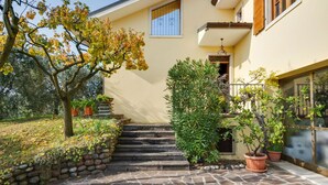 A stone-paved entrance with steps leading to a door, surrounded by potted plants and a tree with autumn leaves. - Modern Holiday Home in Marciaga With Garden (Costermano sul Garda)