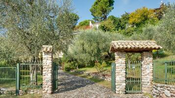 A stone gate with a tiled roof structure, surrounded by greenery and a fence.