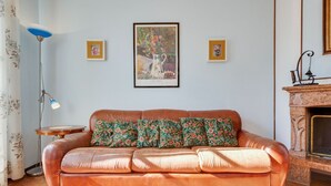 A living room with a brown leather sofa, floral cushions, a framed painting, a floor lamp, and a fireplace. - Modern Holiday Home in Marciaga With Garden (Costermano sul Garda)