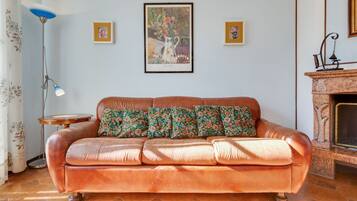 A living room with a brown leather sofa, floral cushions, a framed painting, a floor lamp, and a fireplace.