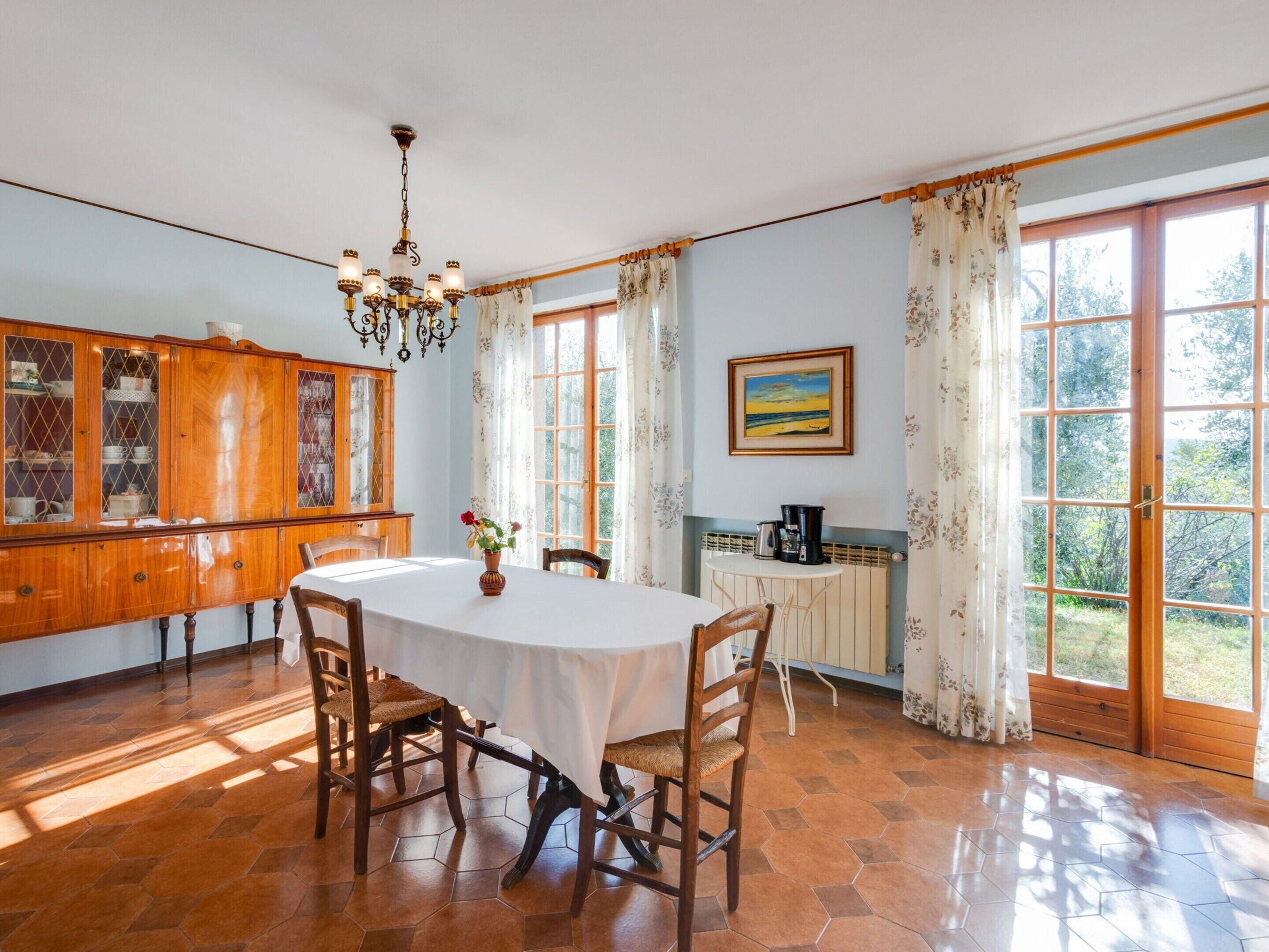 A dining area with a round table, chairs, a chandelier, a cabinet with glass doors, and a painting on the wall.