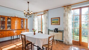 A dining area with a round table, chairs, a chandelier, a cabinet with glass doors, and a painting on the wall. - Modern Holiday Home in Marciaga With Garden (Costermano sul Garda)