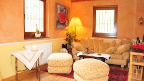 A cozy living room with a sofa, two ottomans, a table with a lamp, and a painting on the wall.